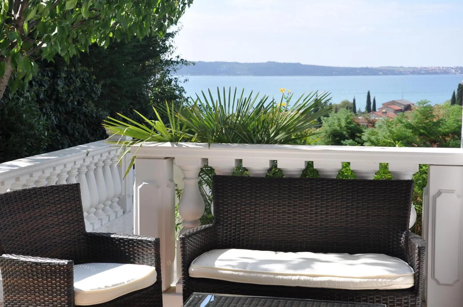 Pokrit balkon apartmaja A z belo balustrado, palmami in morjem v ozadju