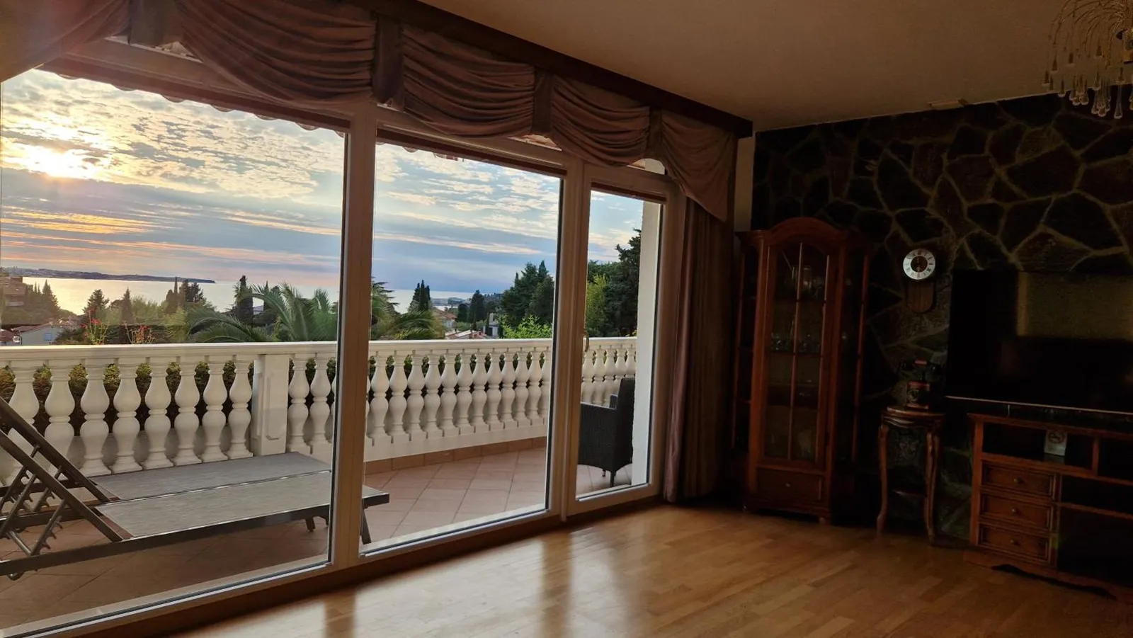 Dnevna soba apartmaja L z veliko steklensko steno in sončnim zahodom nad morjem